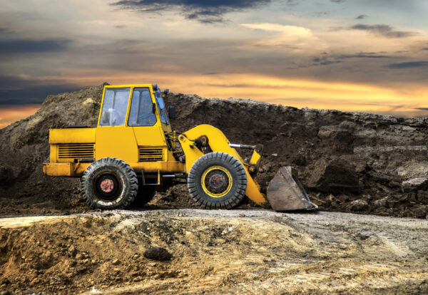 A bulldozer or loader moves the earth at the construction site against the sunset sky. Construction heavy equipment for earthworks