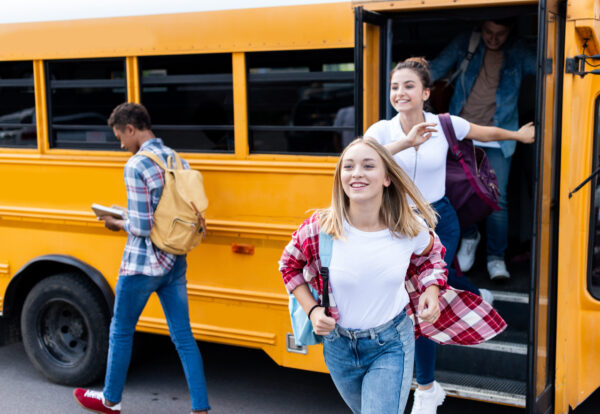 happy multiethnic teen scholars running out school bus
