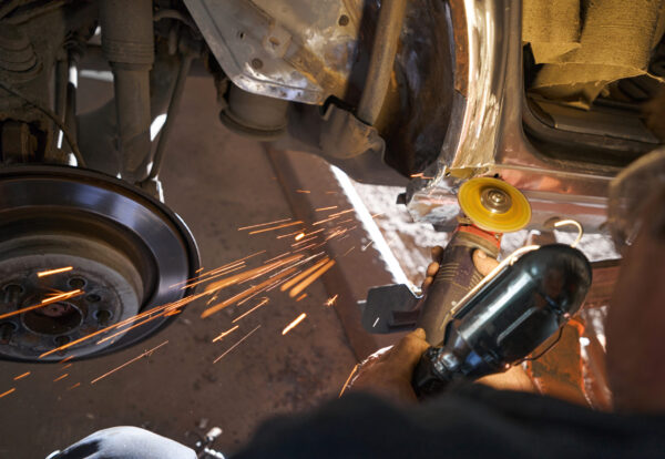 Close-up photo of man working with angle grinder, cleaning welding seams with grinder on car in garage