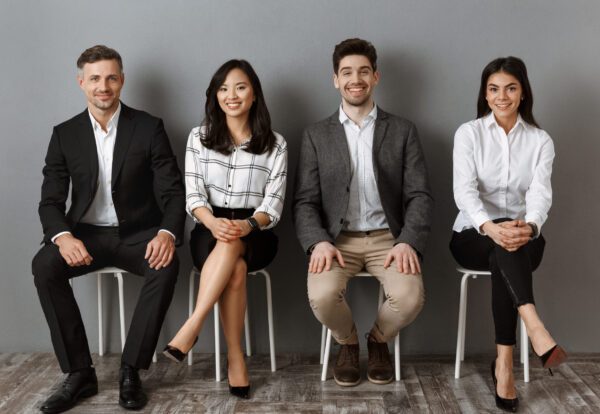 smiling interracial business people in formal wear looking at camera while waiting for job interview
