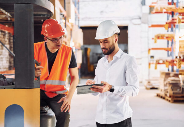 With tablet and cargo moving transport. Two storage workers is in the warehouse.