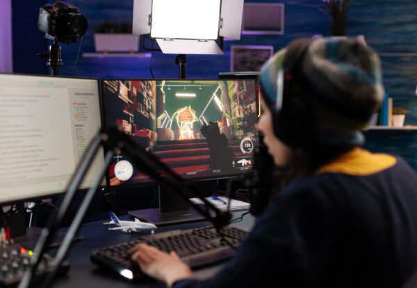 Woman live streaming video games on monitor with chat. Person showing gameplay on online stream, using microphone, headphones and modern equipment to play. Streamer gaming live at desk